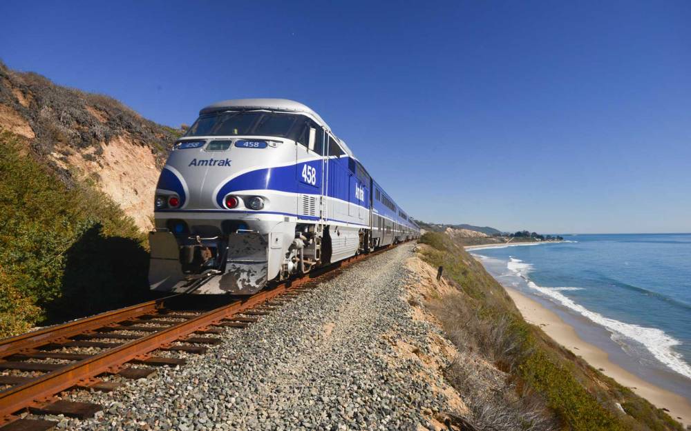 Amtrak Surfliner passenger train on tracks running alongside Pacific Ocean beaches near Santa Barbara on the west coast of California, USA